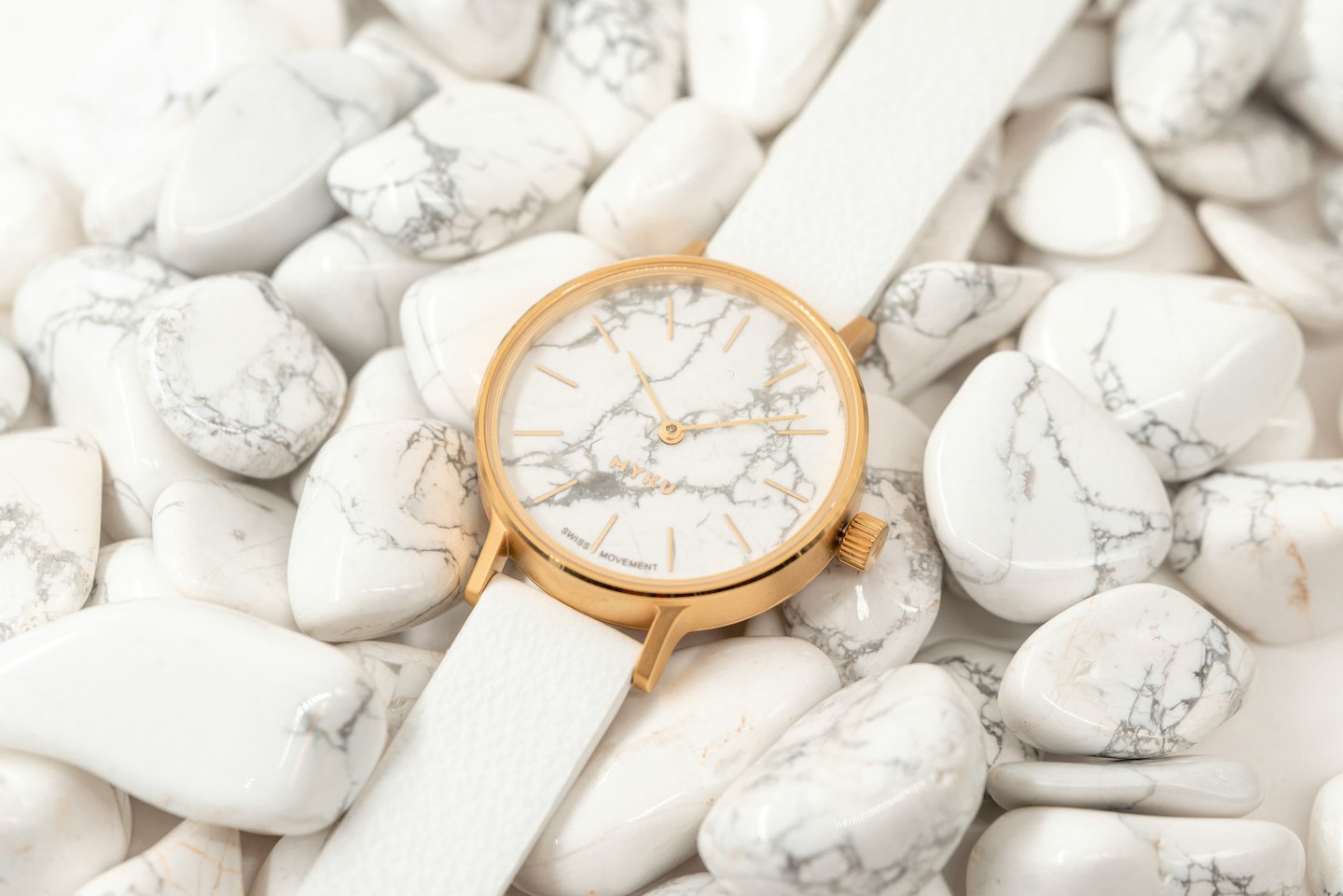Une montre moderne dorée et blanche repose sur des pierres marbrées.