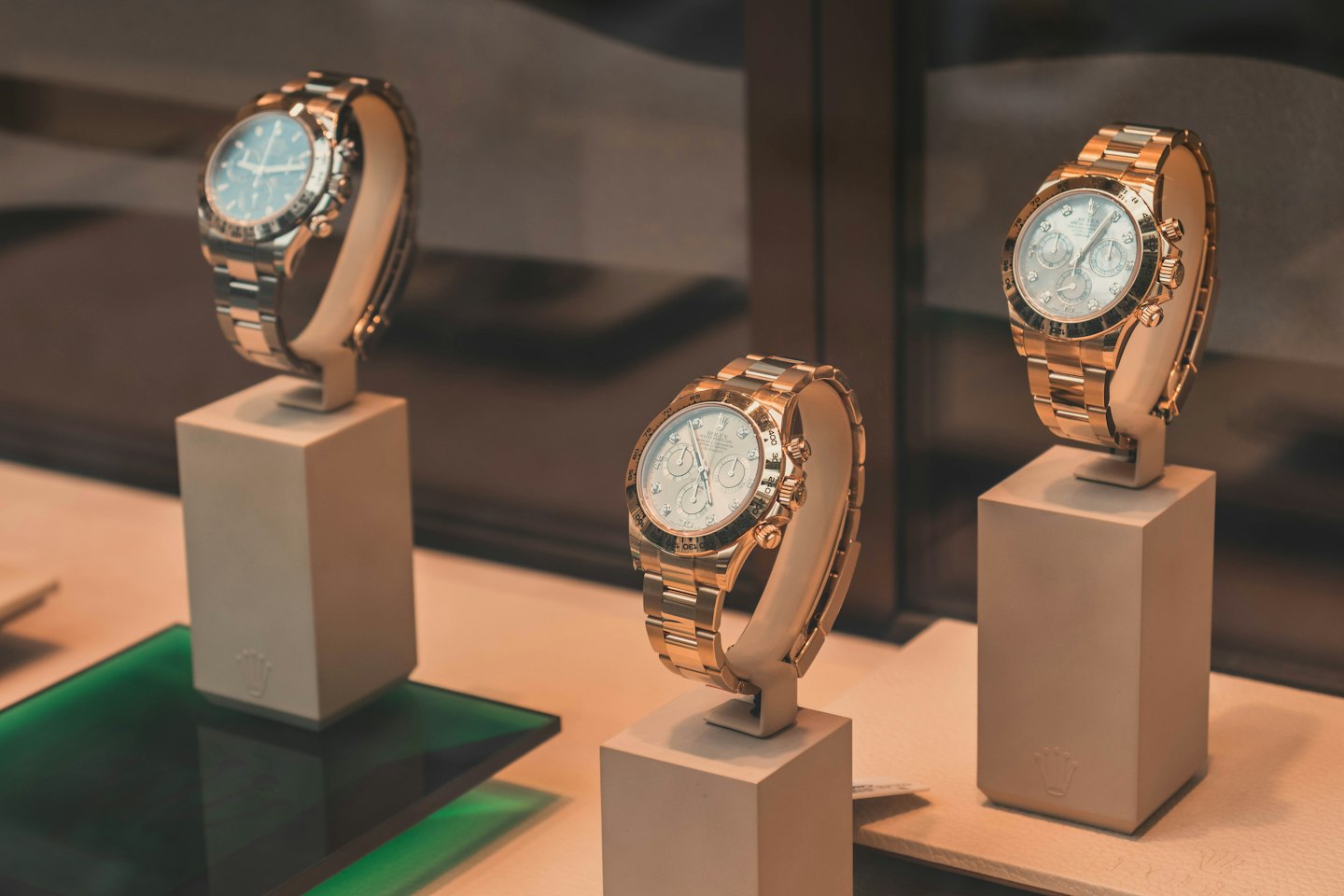 Trois montres de luxe sur des socles beiges dans un magasin.