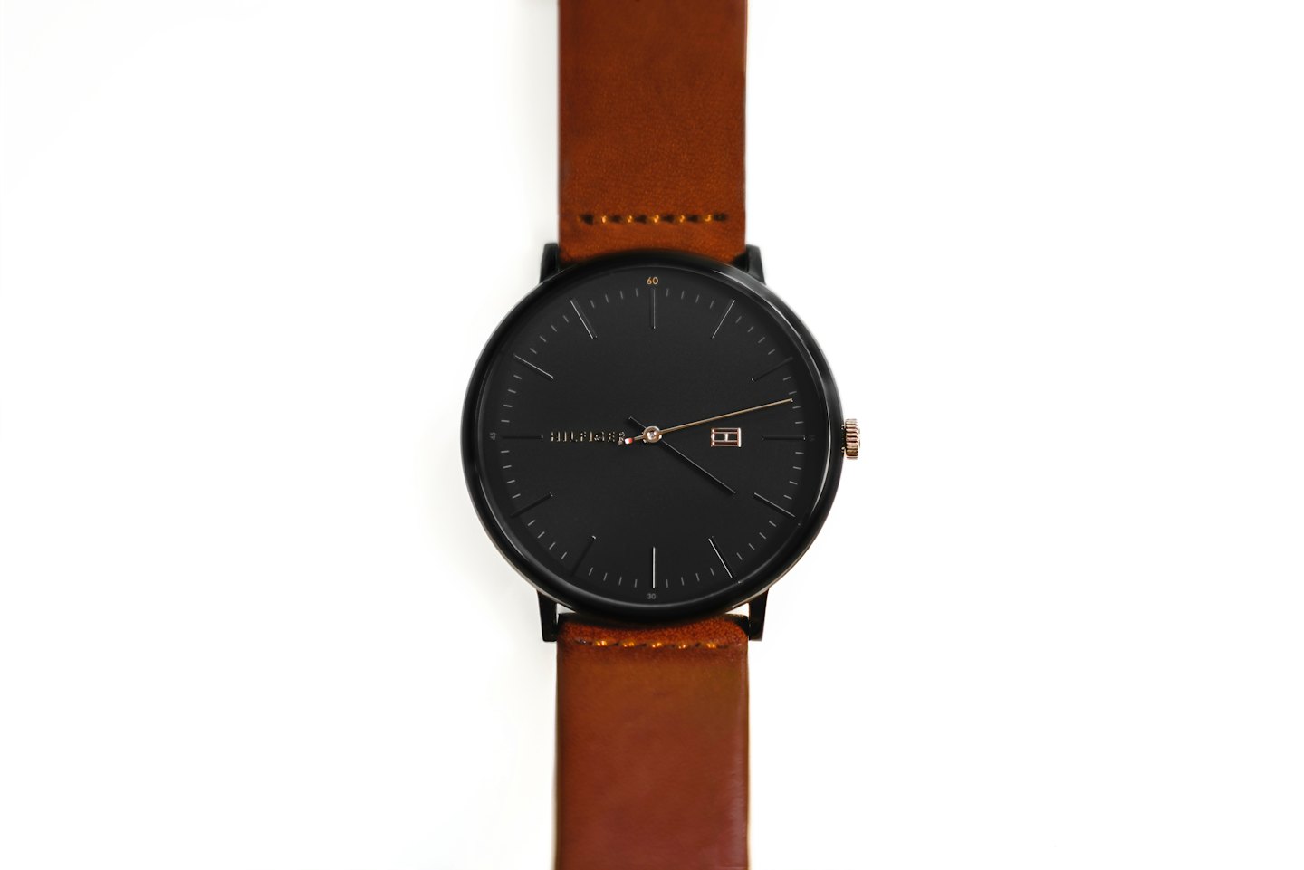 Montre analogique noire avec bracelet en cuir marron sur fond blanc.