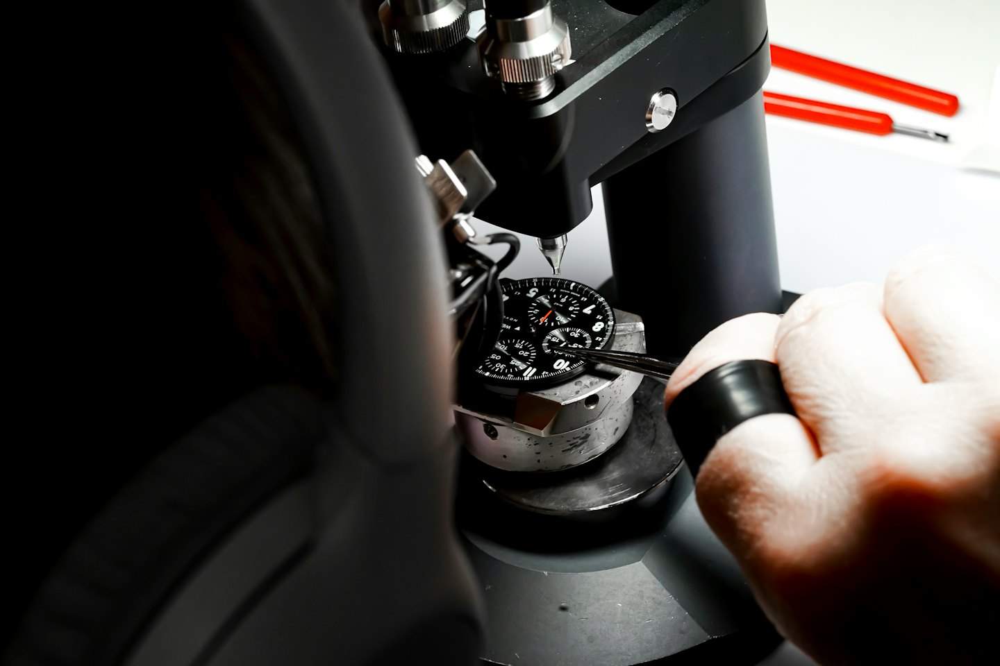 Main d'un horloger ajustant un cadran de montre avec une pince.